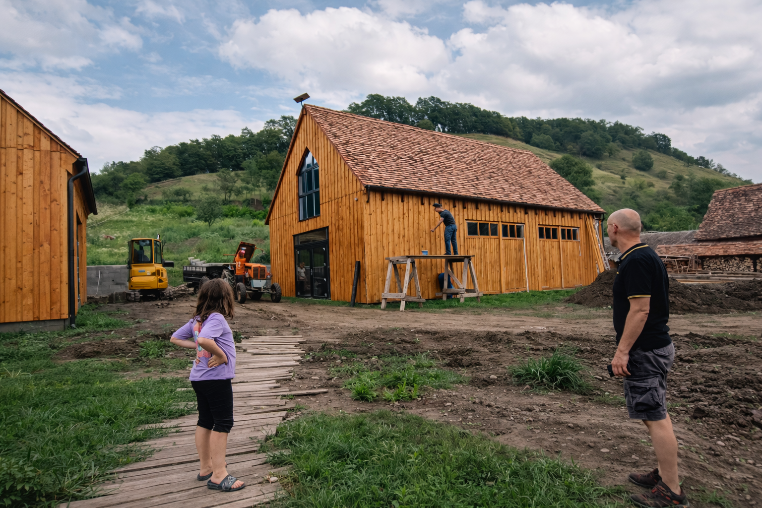 Wooden barn under construction in the Transylvanian countryside, surrounded by green hills and a rural work site